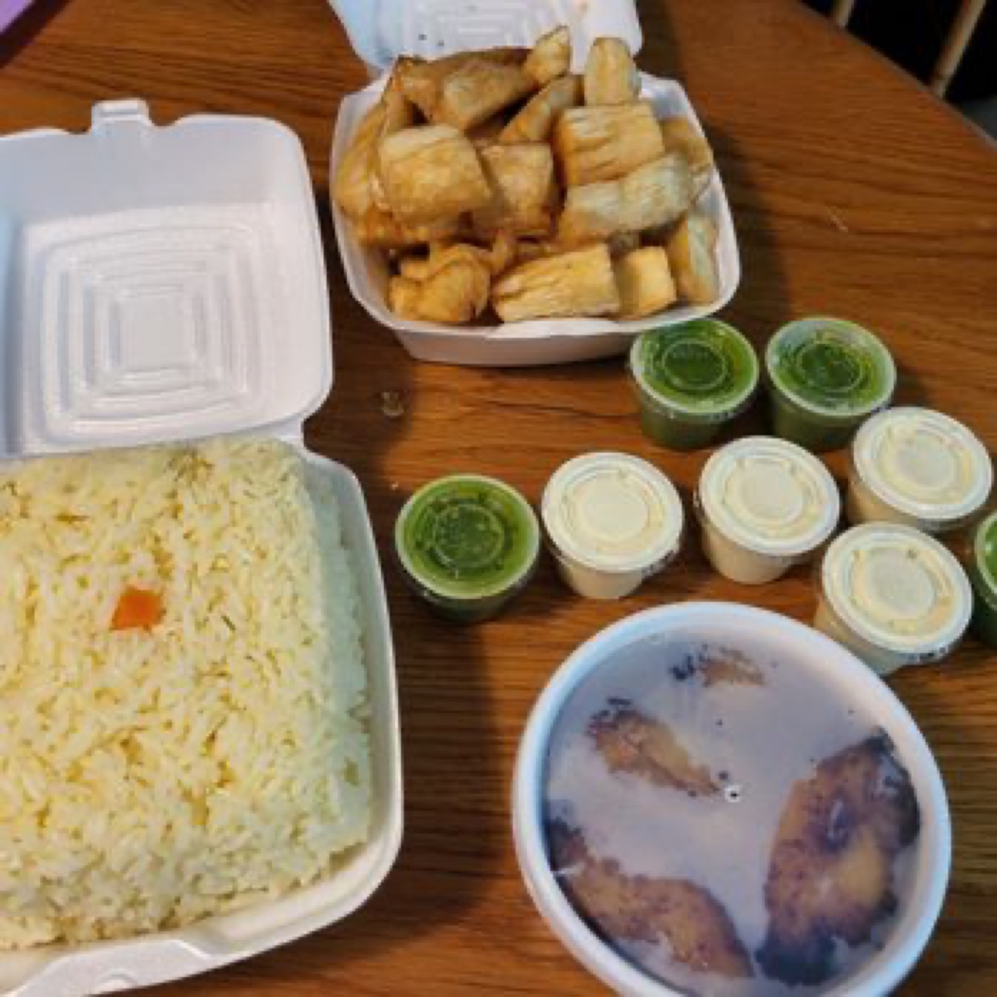 A Chicken Latino takeout spread — rice, yuca, and the signature green aji verde and yellow sauce cups